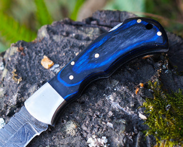 Wooden handle Damascus folding knife on leather surface